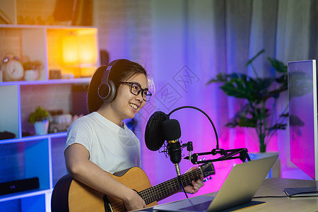 美丽的女孩用耳机唱歌 在家庭录音室用麦克风弹吉他录制新歌音乐家乐趣笔记本吉他娱乐收音机音乐记录青少年电脑图片