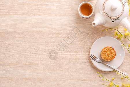 在明亮的木桌上为中秋节准备美味的月饼 喜庆下午茶的概念装饰着黄色花朵 顶层视野 平铺小吃盘子糕点桌子茶壶蛋糕木头节日食物杯子图片