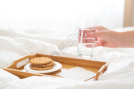 女性手在托盘上举着水杯 床上装着饼干玻璃节食白色饮食桌子食物营养图片