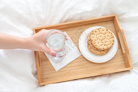 女性手在托盘上举着水杯 床上装着饼干桌子玻璃白色饮食节食食物营养图片