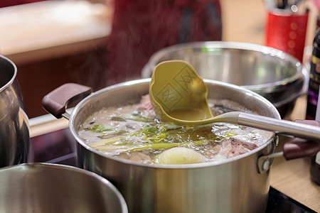 锅里装满了沸腾的蔬菜和肉汤的金属酱 在汤里有勺子图片