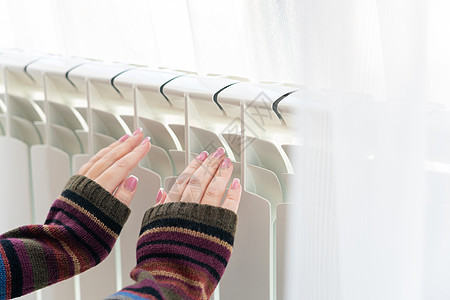 女孩把冷冻的手放在热散热器上加热器毛衣房子白色技术经济控制加热家庭温暖图片