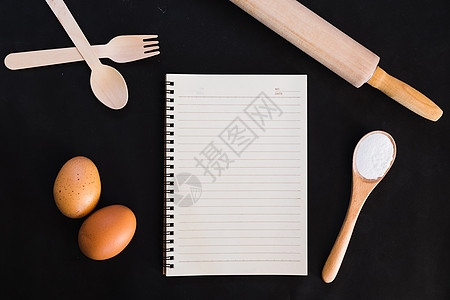 烘烤蛋糕配料 食谱书 勺子 面粉 鸡蛋 打蛋器 滚针和蛋壳在黑桌上图片