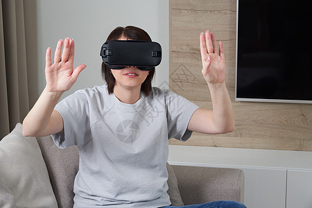 快乐的年轻女人在室内玩 VR 眼镜虚拟现实概念与年轻女孩玩耳机护目镜和复制空间长椅展示乐趣女士模拟模拟器享受女性视频沙发图片