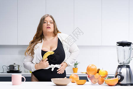 饮食和营养概念 快乐的卷曲身体年轻女子 长金发长发 在现代厨房使用搅拌机 将新鲜果子混合起来用于健康溜冰烹饪小吃食物肥胖午餐脂肪图片