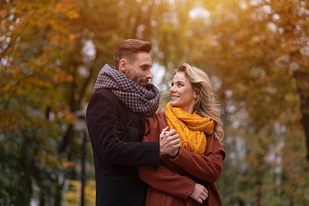 一对热恋中的情侣的画像 在秋天的公园里 英俊的男人和女人从背后拥抱 微笑着看着对方 一对热恋中的年轻夫妇玩得很开心的户外照片 秋图片