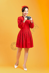 全身美丽的亚洲年轻美女 穿着红色礼服 在工作室里以橙色背景 手上拿着摄像头图片