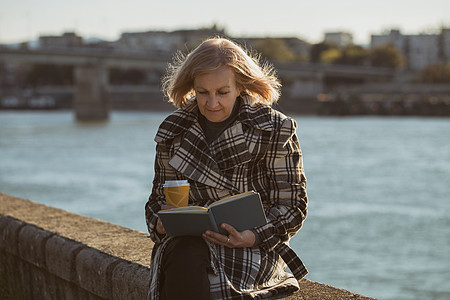 年长妇女阅读书和喝咖啡图片