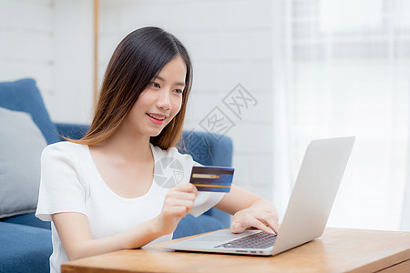 年轻的亚洲女性坐在沙发上 使用笔记本电脑在线购物 信用卡购买互联网 快乐的女孩在沙发上通过电子商务付款 购买和付款 商业理念闲暇图片