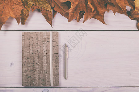 带秋叶的木制桌边笔记本和笔公告季节教育笔记棕色褐色作品日记记事本写作图片