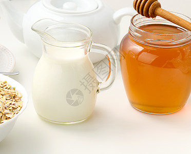 新鲜牛奶 一个透明的玻璃脱盐机和一罐蜂蜜摊在白桌上 一种健康的产品 早餐图片