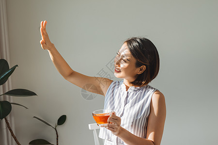 一个满意的女人的肖像 看着一面 一边拿着茶杯 站在家里的窗户旁边乐趣微笑饮料女士成人女孩图片