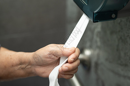亚洲年长的老年老妇病人在护理医院病房厕所洗手间把组织从卷子上拉出来图片