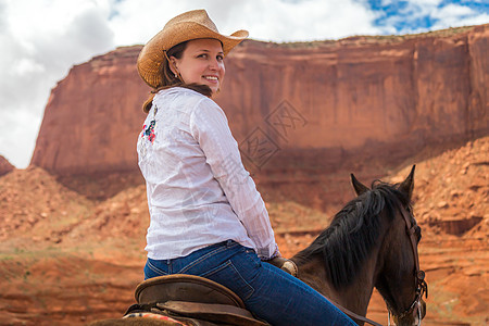 在古迹谷骑马时身戴草帽的牛仔女郎侵蚀石头天空悬崖稻草旅游沙漠荒野山丘女孩图片