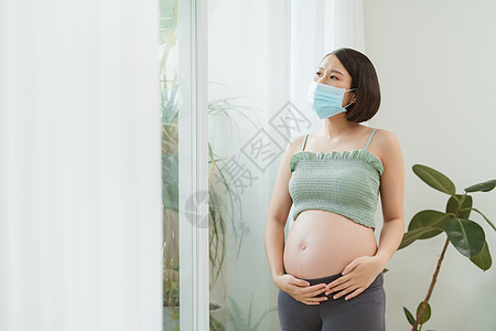 身戴医疗面具的年轻怀孕女年青身孕女性 独自呆在家中进行自我隔离图片