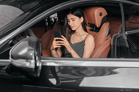 年轻有吸引力的亚洲女性坐在豪华轿车前海边使用电话旅行商务奢华汽车手机沙龙车辆座位司机女孩图片