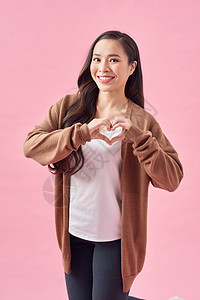 快乐的女人用她的双手塑造心型 粉红色背景的特写肖像图片