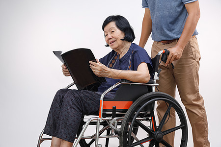 与儿子一起看轮椅的书的老年妇女要小心男人杂志照顾者祖母女士母亲退休男性家庭幸福图片