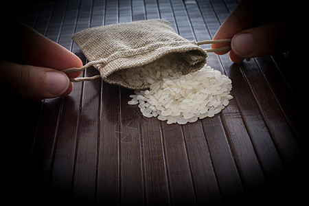 手持草袋 用木制背景装满未煮熟的米饭口袋种子稻草谷物食物木头粮食营养香米宏观图片
