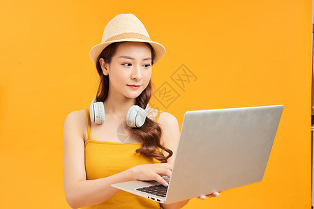 穿黄色夏季服装的旅游女游客 用笔记本电脑耳机在橙色背景上隔绝图片