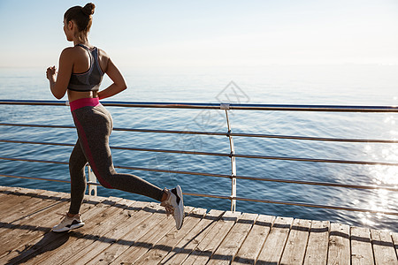 观察女性运动员在海边赛道上锻炼 在海边慢跑福利有氧运动天空阳光训练码头成人行动赛跑者女孩图片