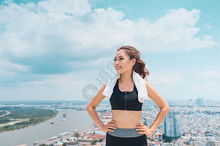 穿着运动服的年轻女子在蓝天上站在屋顶上微笑身体健康瑜伽训练蓝色城市运动天空女性女孩图片