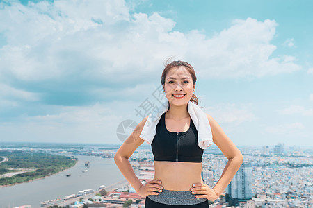 穿着运动服的年轻女子在蓝天上站在屋顶上微笑运动蓝色女性训练健康城市瑜伽身体女孩天空图片