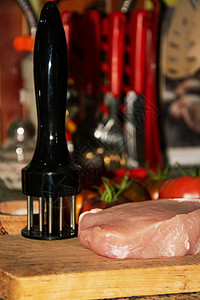一块生猪肉放在厨房桌子上的木砧板上的肉类软化剂旁边图片
