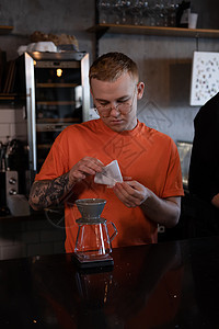 穿着橙色T恤的金发男子 准备替代咖啡酿制 现代阁楼咖啡店中的化学施工商业职员服务员化学试剂酿造饮料冲泡橙子店铺图片