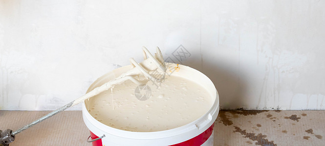 桶里的白色油漆 地板上有搅拌器 房间里有一桶白色油漆 家装理念图片