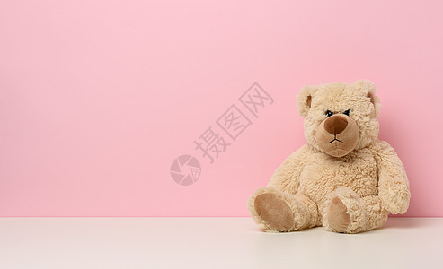 棕褐色的泰迪熊面带悲伤的脸 坐在白桌上 粉红背景图片