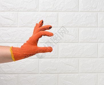 白砖墙背景下 戴着橙色工作防护手套的女手 手有条件地握着一个物体女士手指衣服橙子配饰家庭黑色材料工业纺织品图片