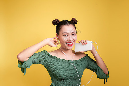 在黄色背景下用耳机收听音乐的时装 微笑着笑容的女性女性喜悦幸福快乐青少年乐趣唱歌青年女士音乐图片