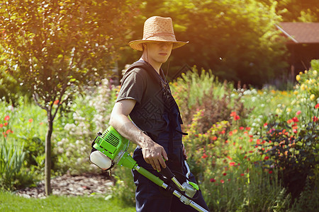一个年轻男子带着割草机 照顾后院的草地男人院子工人园艺工作园丁刀具帽子修剪生长图片