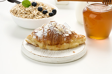 涂满糖粉的烤面包羊角面包 在白桌上一个陶瓷板中的燕麦片 早餐图片