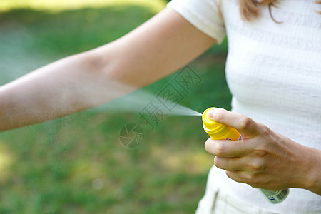 年轻女性在自然活动期间对手臂施用驱蚊剂;昆虫驱虫剂;防虱子和其他昆虫的皮肤保护;关注喷雾容器顶部图片