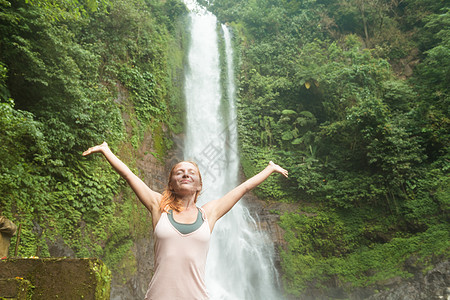 在瀑布边做瑜伽的年轻女子女士白色冥想生活福利岩石专注女孩闲暇沉思图片