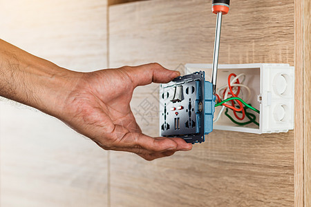 电工的手正在使用螺丝刀将电线连接到带有 USB 端口的通用墙壁插座交流电源插头 并在木墙上的塑料盒中开关图片