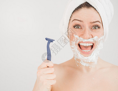 可爱的女人 头上戴毛巾 脸上有剃须泡沫 在白色背景上拿着剃刀浴室卫生奶油治疗头发美容师女孩刀刃沙龙浴缸图片