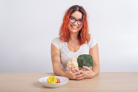 白种女人更喜欢健康的食物 红发女孩在西兰花和甜甜圈之间选择白种背景脂肪活力薯条垃圾蔬菜微笑饮食卫生女孩甜点图片