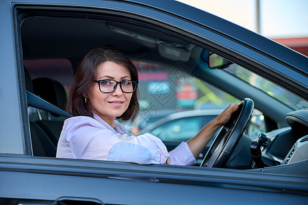 驾驶汽车的中年年轻 美丽的女性司机窗户微笑眼镜座位越野车车辆腰带交通成人人士图片