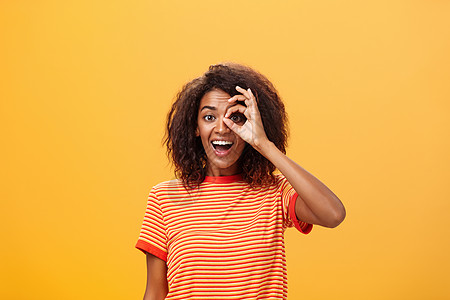 穿着条纹T恤衫的卷发丝发型 在眼睛上环绕或笑着微笑 广泛准备参加橙墙附近的探险活动 Y L 18头发广告冒险卷曲女孩女性情绪学生图片