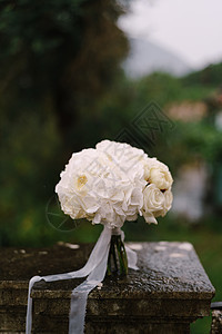 白色玫瑰和礼服的鲜白新娘花束 湿石栏杆上带白丝带背景图片