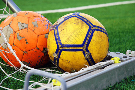 两个衣衫褴褛的足球躺在球门的角落里 反对绿色足球场图片