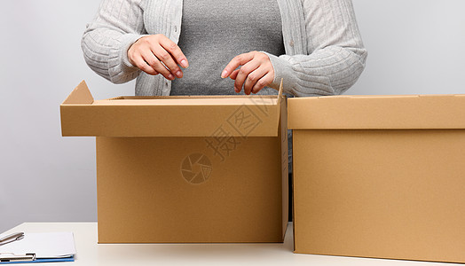 身着灰色衣服的妇女站着 在白色背景 移动 发送和运送货物上持有开放的棕色盒子导游运输公寓送货工作服务包装邮政女士仓库图片