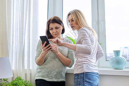 两位中年女性朋友一起看智能手机屏幕 在网上观看工具喜悦女士技术朋友们窗户互联网闲暇阅读电话图片