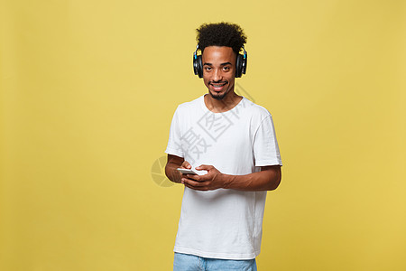 黑人年轻人在耳机上听音乐 在黄色背景上被孤立的一无所有金子乐趣男人微笑幸福技术成人男性快乐男生图片