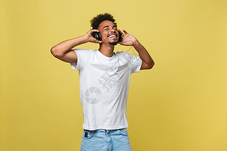 黑人年轻人在耳机上听音乐 在黄色背景上被孤立的一无所有男生快乐文化技术青年冒充玩家夹克衬衫工作室图片