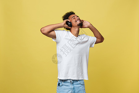 非裔非洲青年男子戴耳机 在黄色金色背景上享受音乐与黄金背景相比国家成人头发幸福爆炸歌曲舞蹈乐趣玩家工作室图片