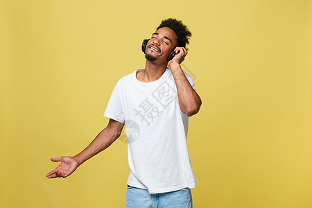 黑人年轻人在耳机上听音乐 在黄色背景上被孤立的一无所有工作室冒充闲暇金子衬衫男生文化成人幸福多样性图片